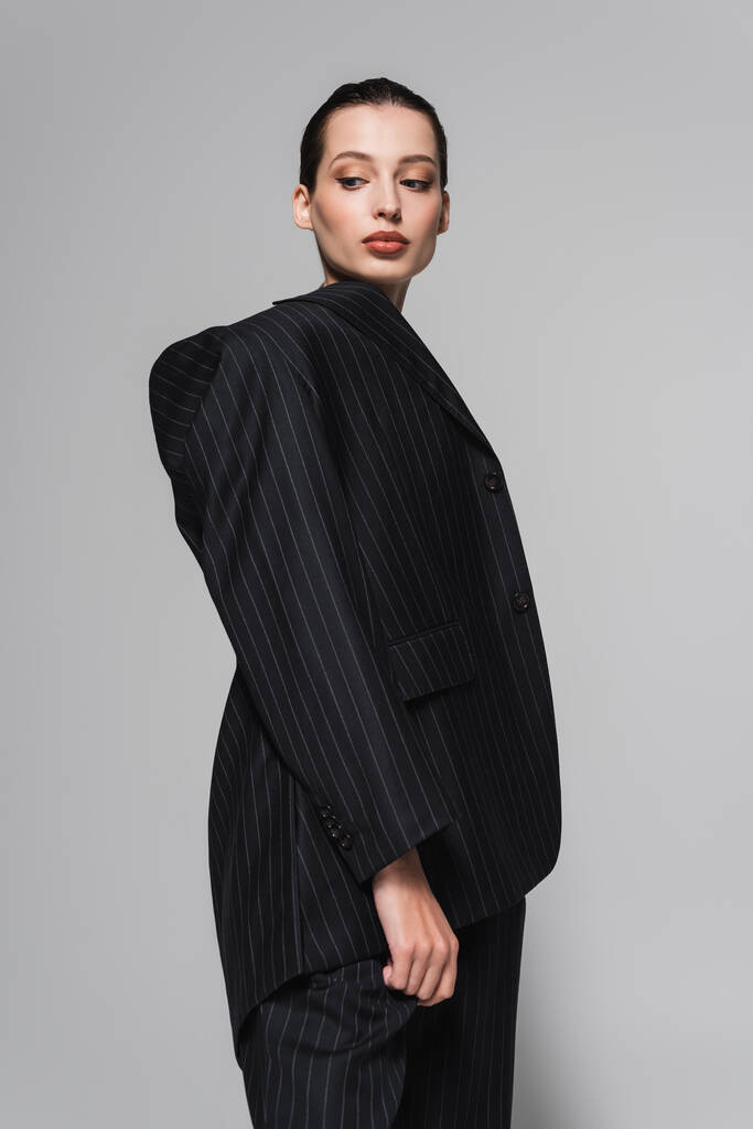Low angle view of pretty woman in black suit looking away isolated on grey  - Photo, Image