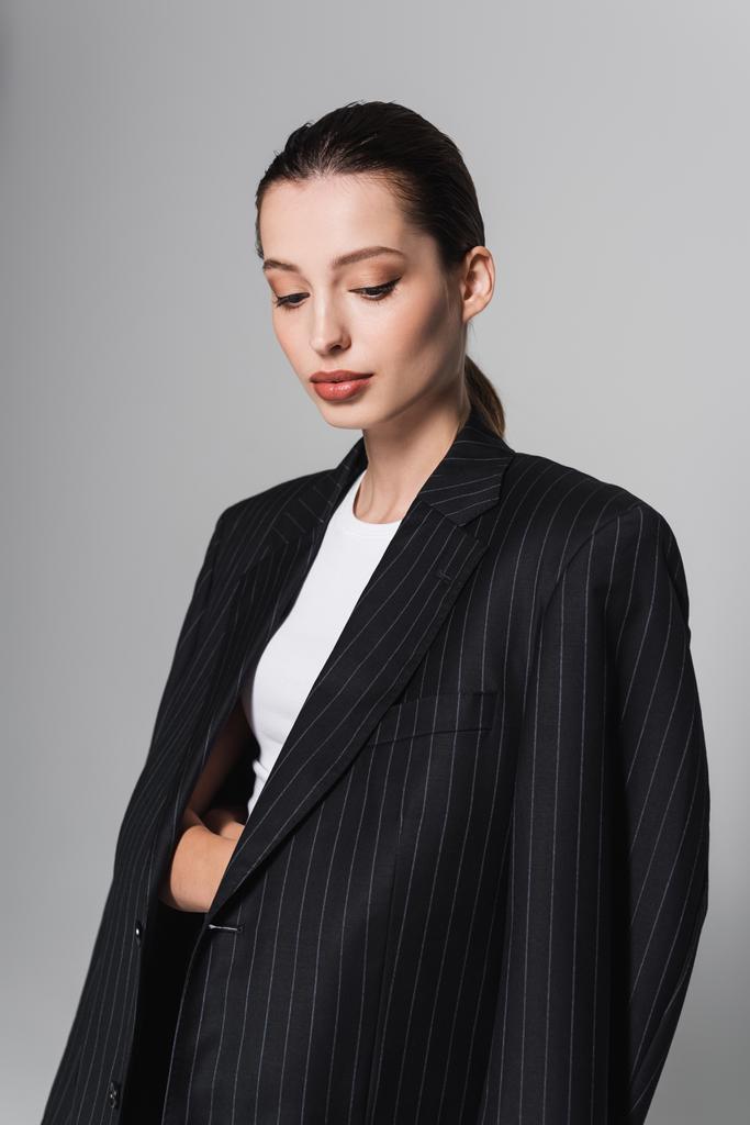 Tyylikäs nainen meikki poseeraa musta takki eristetty harmaa  - Valokuva, kuva