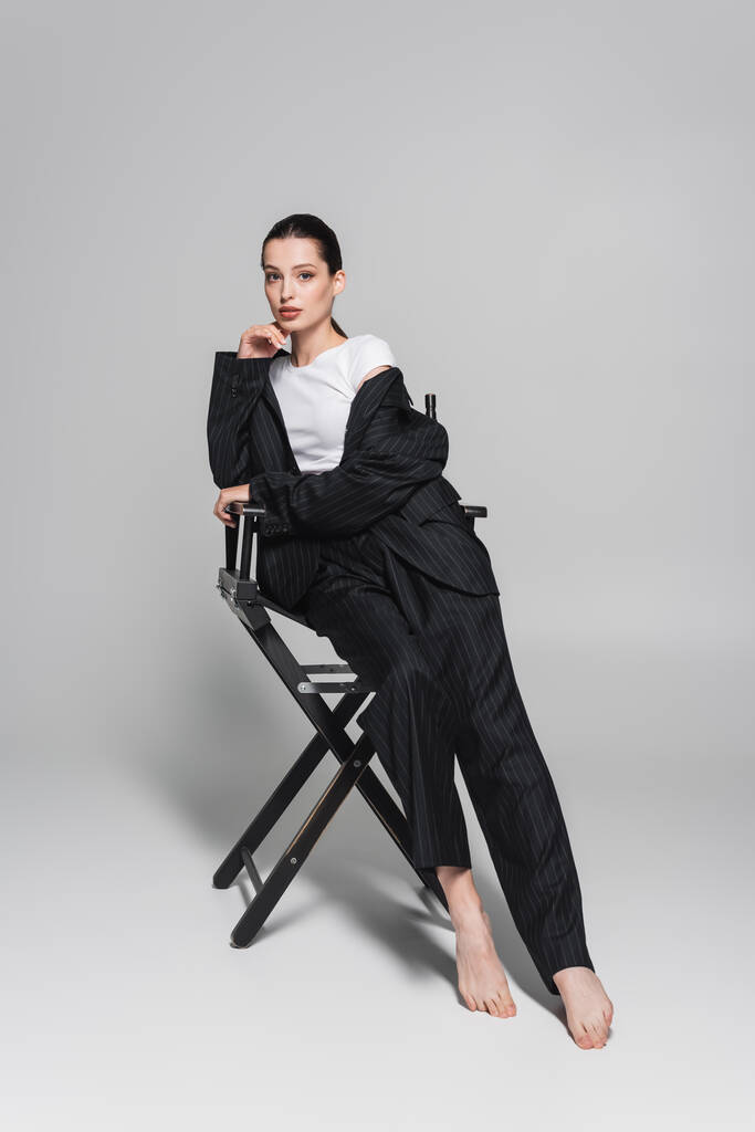 Mezítláb modell csíkos öltöny és póló ül összecsukható szék szürke alapon  - Fotó, kép