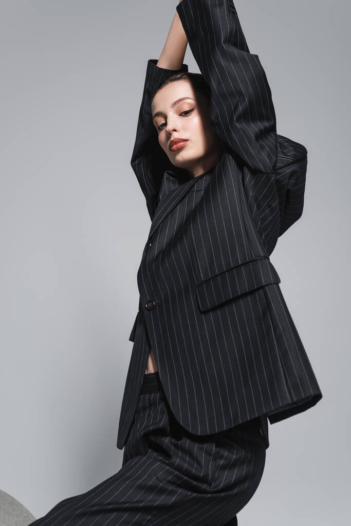 Mujer joven de moda con maquillaje en traje negro posando aislado en gris  - Foto, Imagen