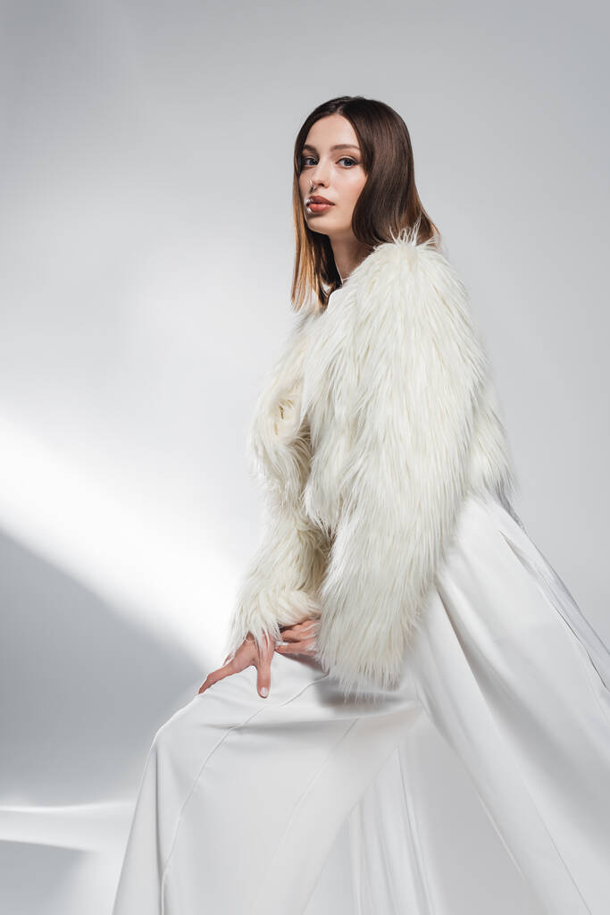トレンドモデルで白い服とフェイクファージャケット見てカメラで抽象的なグレーの背景  - 写真・画像