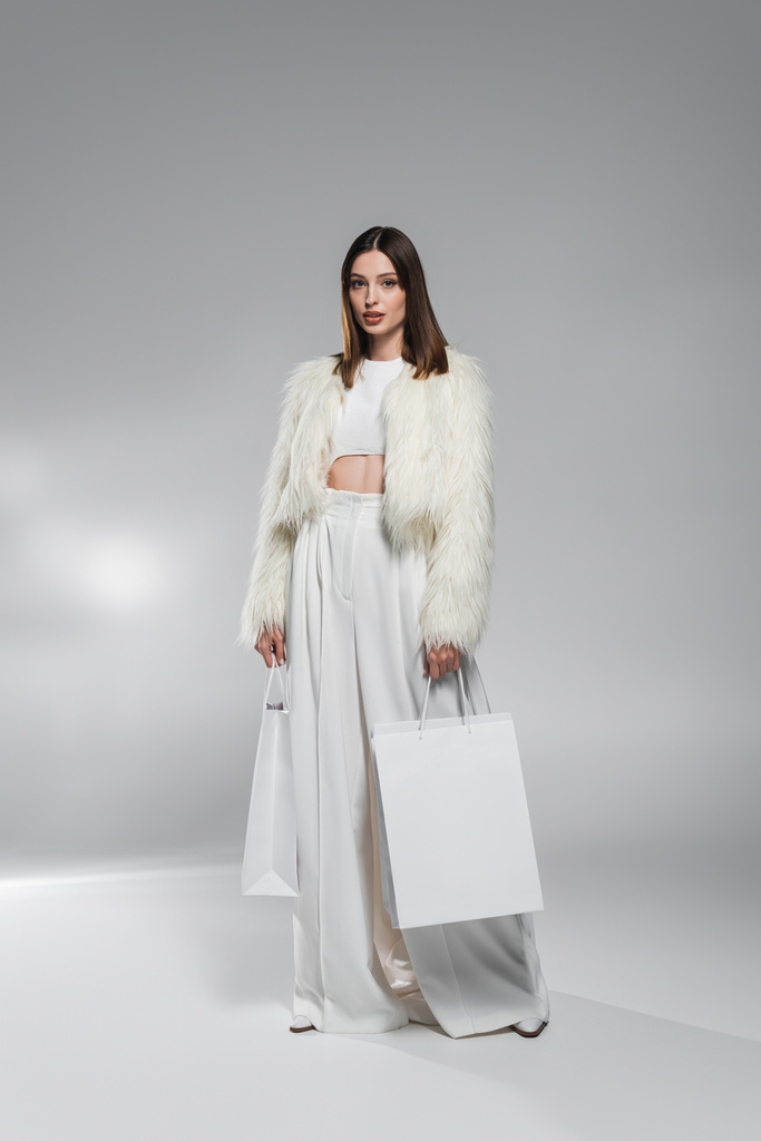 ショッピングバッグを持つ白い服の流行の女性の完全な長さ抽象的な灰色の背景  - 写真・画像