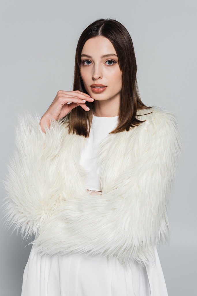 portret van mooie jonge vrouw in stijlvolle witte faux fur jas op zoek naar camera geïsoleerd op grijs - Foto, afbeelding
