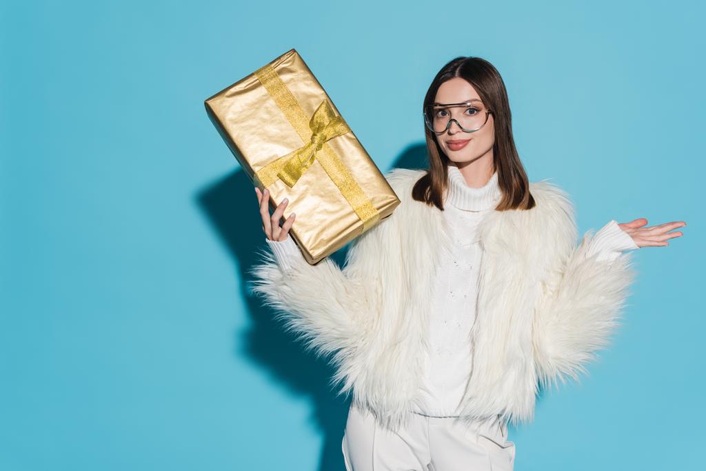 stílusos nő faux szőrme kabát és szemüveg gazdaság karácsony ajándék kék háttér - Fotó, kép