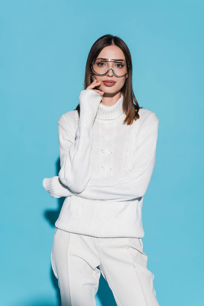 pretty young woman in eyeglasses and white turtleneck looking at camera on blue - Photo, Image