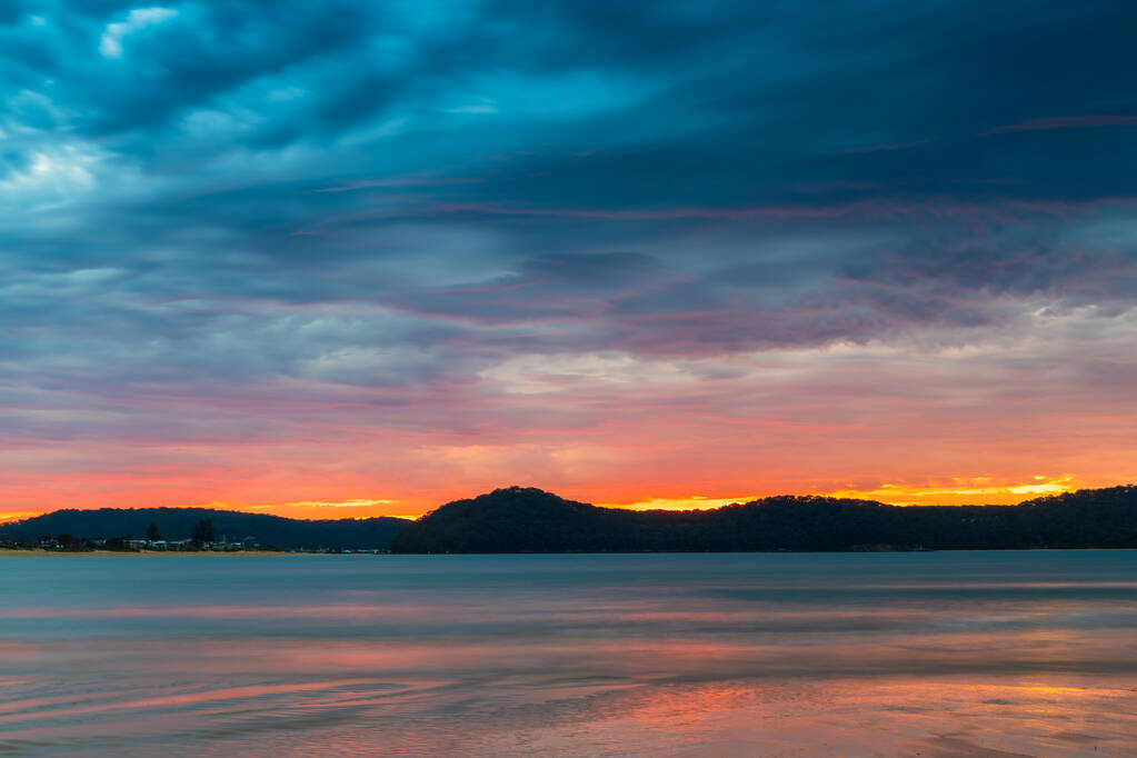 Sunrise at the beach with colourful high cloud filled sky and flat surf at Umina Point, Umina Beach on the Central Coast, NSW, Australia. - 写真・画像