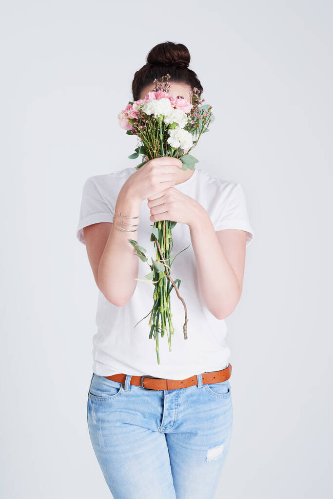 Είναι εύκολο να κρυφτεί πίσω από όμορφα λουλούδια. Στιγμιότυπο στούντιο μιας αγνώριστης γυναίκας που καλύπτει το πρόσωπό της με λουλούδια σε γκρι φόντο - Φωτογραφία, εικόνα