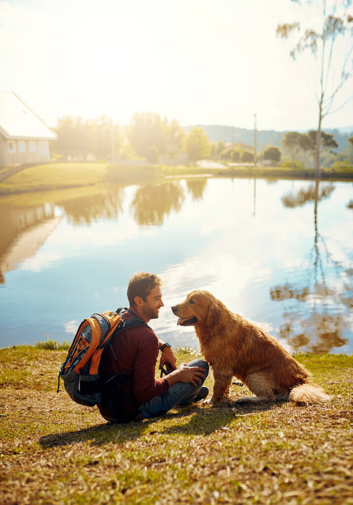 Hes definitely this mans best friend. Full length shot of a handsome young man and his dog sitting by a lake in the park - Photo, Image