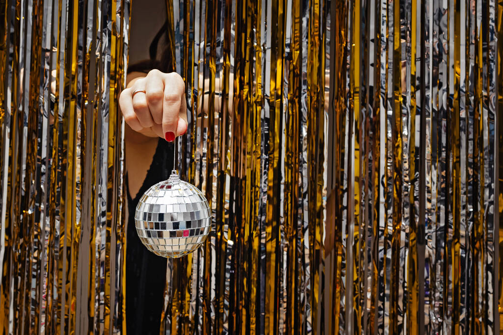 Mão da mulher segurando bola de discoteca decorativa através das cortinas brilhantes - Foto, Imagem