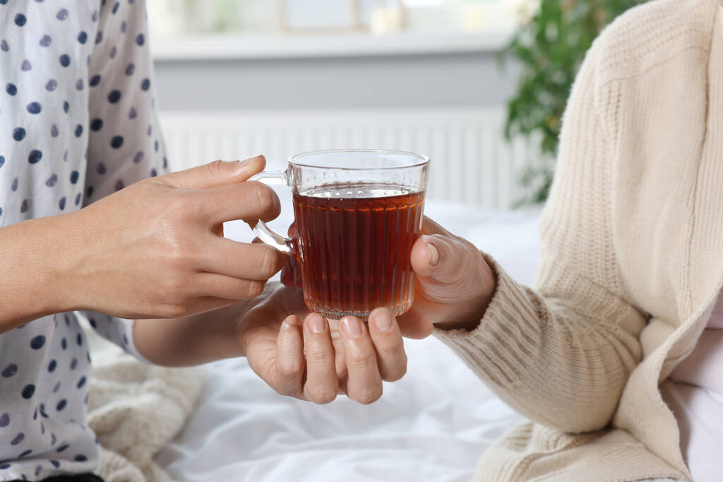 Pflegerin gibt älteren Frau zu Hause Tee, Nahaufnahme - Foto, Bild