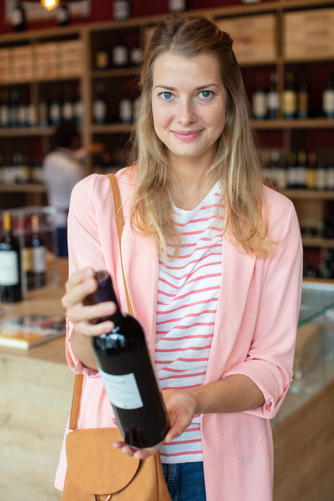 Satın almak için hangi şişe şarap karar vermeye çalışan kadın - Fotoğraf, Görsel