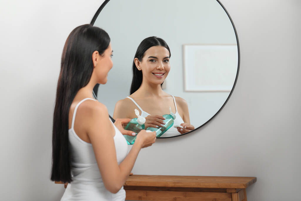 Jeune femme versant de l'eau micellaire sur un coton près d'un miroir à l'intérieur - Photo, image