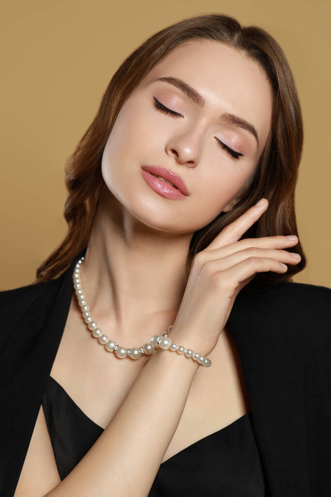 Giovane donna che indossa eleganti gioielli di perle su sfondo marrone - Foto, immagini