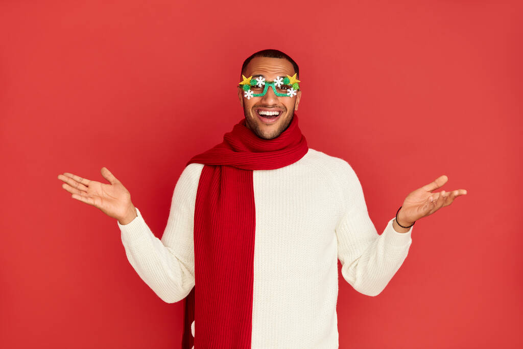 Shrugging Man Smiling Studio. Confused Multiracial Guy Standing with No Idea Gesture, Shrugging Shoulders Raising Hands. New Year Concept. Indoor Studio Shot Isolated on Red Background  - Photo, Image