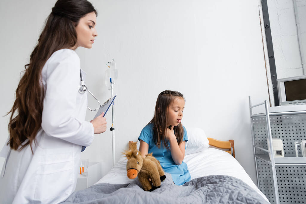 Gyerek köhögés közelében gyermekorvos írótáblával a klinikán  - Fotó, kép