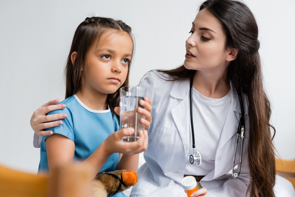 Lekarz trzyma tabletki i rozmawia z dziewczyną ze szklanką wody na oddziale szpitalnym.  - Zdjęcie, obraz