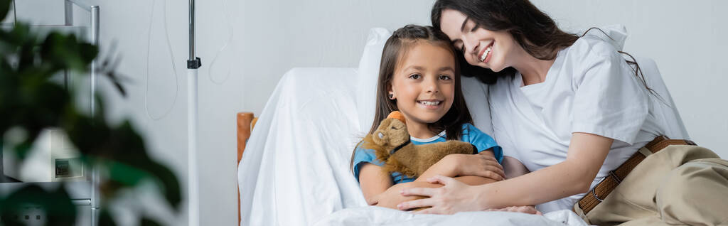 Fiatal anya ölelés gyermek puha játék az ágyon kórházi kórteremben, banner  - Fotó, kép