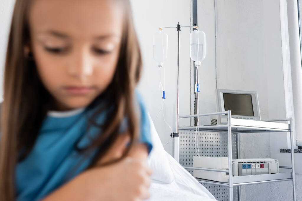 Внутривенная терапия на стенде рядом с размытым ребенком в больничном платье в клинике  - Фото, изображение