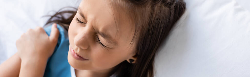 Υψηλή γωνία άποψη του άρρωστου παιδιού αγγίζοντας ώμο, ενώ βρίσκεται στο κρεβάτι στο θάλαμο του νοσοκομείου, πανό  - Φωτογραφία, εικόνα