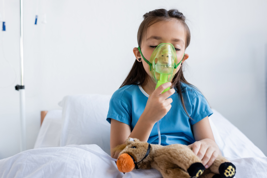 Bambino malato con maschera di ossigeno vicino giocattolo sul letto in ospedale  - Foto, immagini