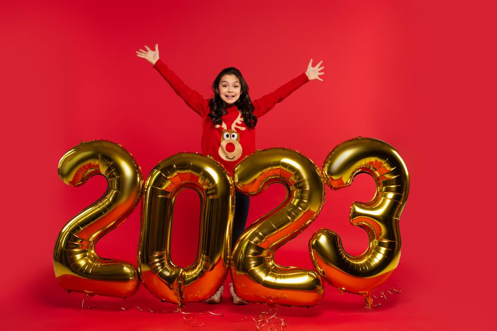 pleine longueur de fille excitée en pull debout près de ballons avec 2023 numéros sur rouge - Photo, image