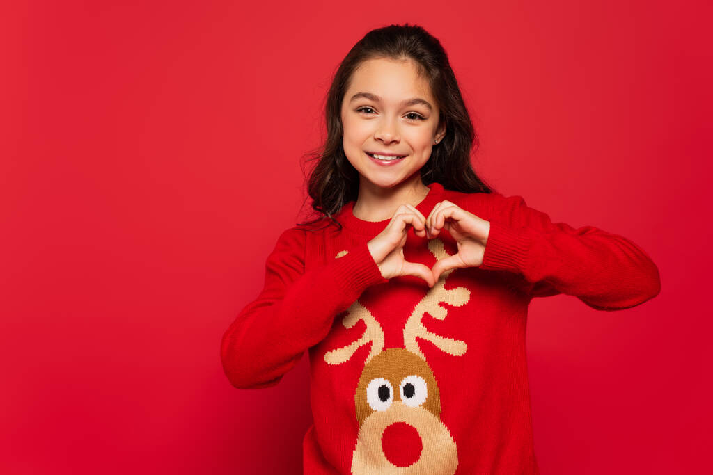 χαρούμενο παιδί το χειμώνα πουλόβερ δείχνει την καρδιά σημάδι με τα χέρια απομονώνονται στο κόκκινο - Φωτογραφία, εικόνα