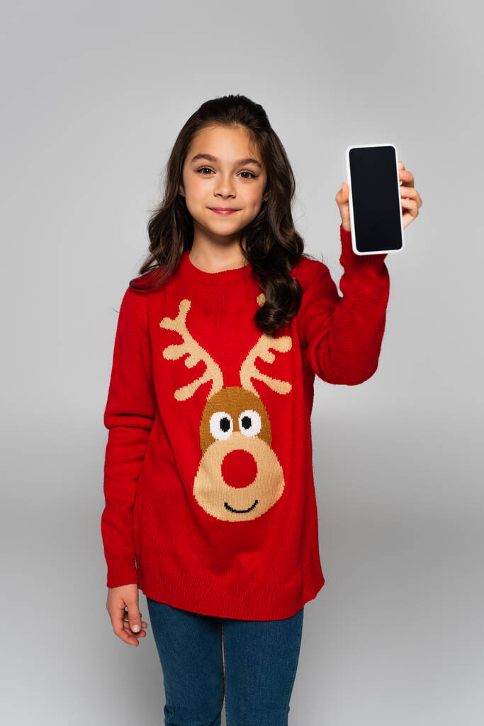 Menina pré-adolescente em camisola de Natal segurando smartphone isolado em cinza  - Foto, Imagem