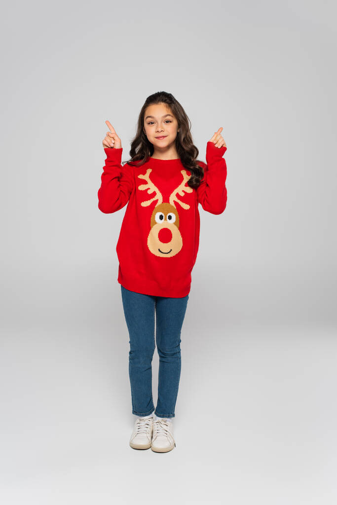 Comprimento total da criança em suéter de ano novo apontando com os dedos no fundo cinza  - Foto, Imagem