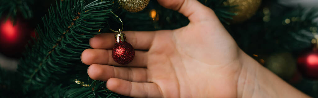 Vista ritagliata del bambino che tocca la palla festiva sull'albero di Natale, banner  - Foto, immagini