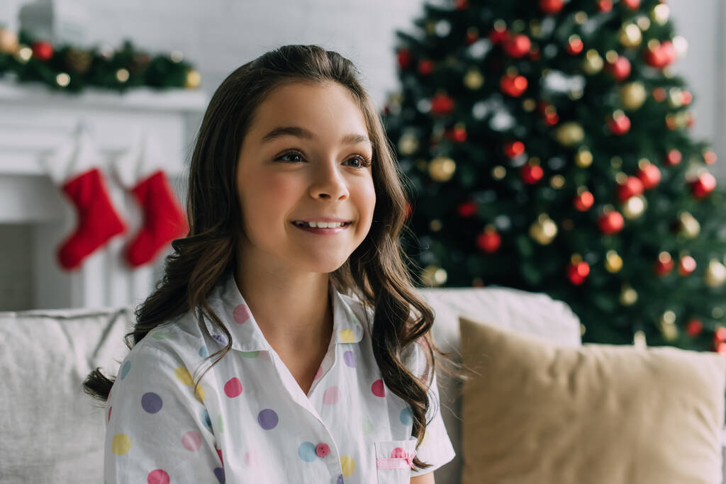 Χαμογελώντας παιδί στην πιτζάμα κοιτάζοντας μακριά κατά τη διάρκεια των Χριστουγέννων γιορτή στο σπίτι  - Φωτογραφία, εικόνα