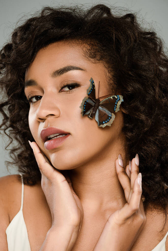 довольно африканская американка с бабочкой на лице, изолированной от серых - Фото, изображение