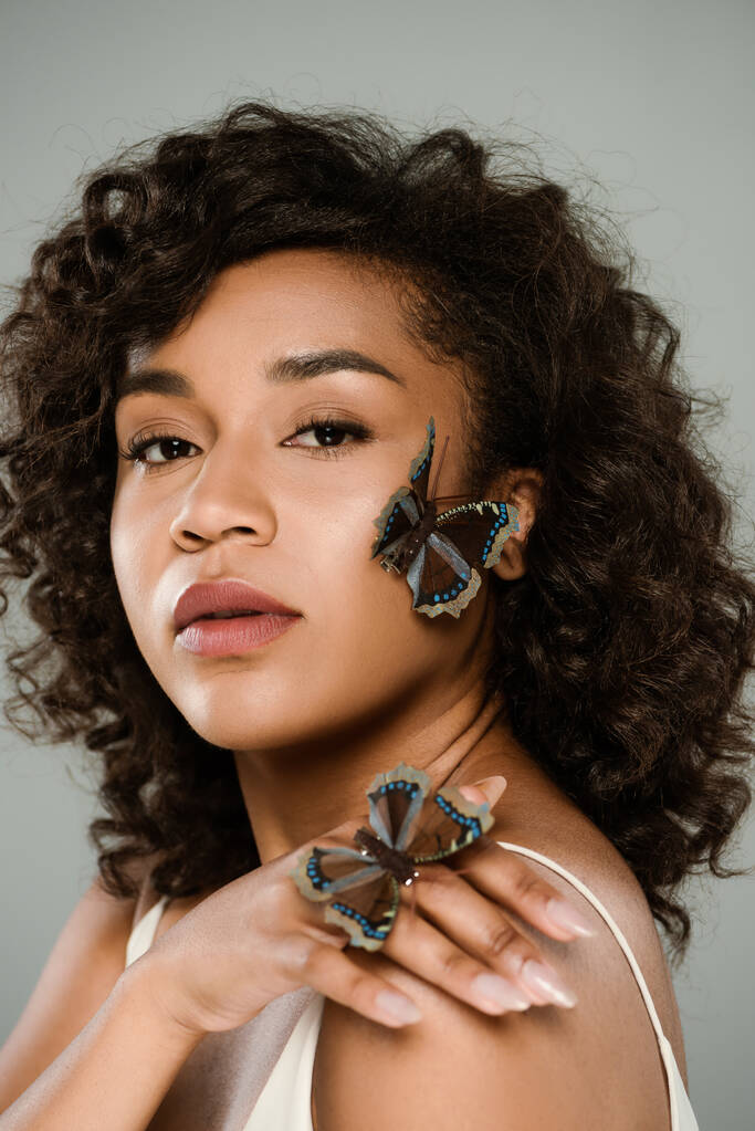 afro-amerikai nő pillangókkal a kezén és az arcán a szürke kamerát nézi. - Fotó, kép