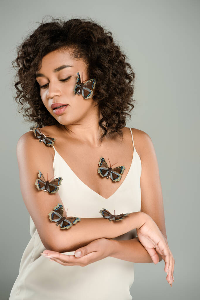 Vücudunda kelebekler olan kıvırcık saçlı Afrikalı Amerikalı kadın gri renkte izole edilmiş.  - Fotoğraf, Görsel