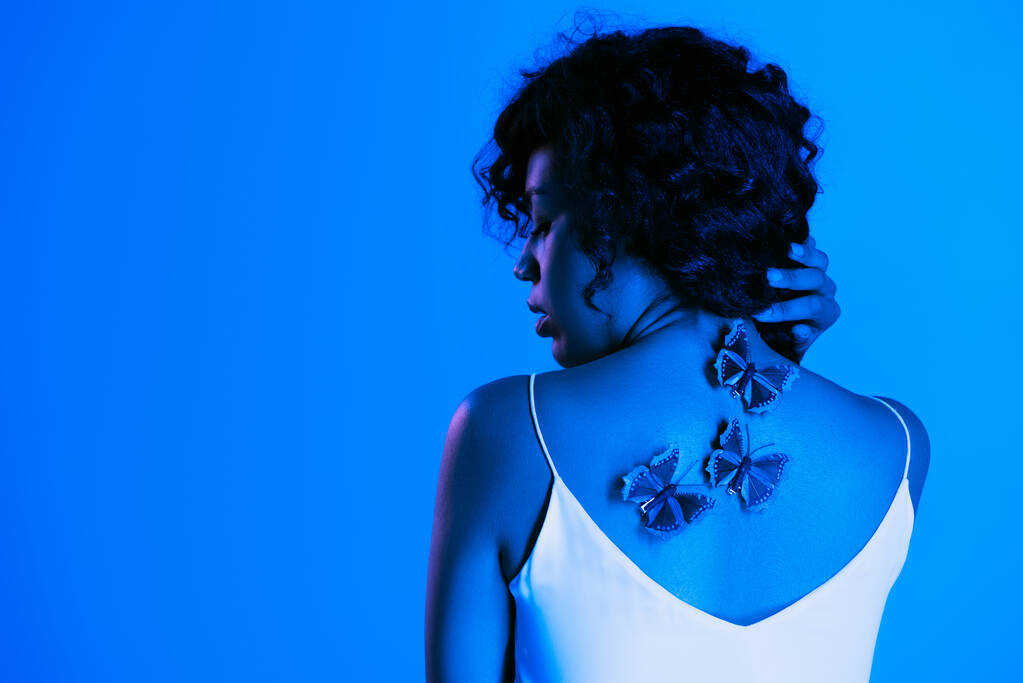 fiatal afro-amerikai nő pillangók hátán pózol elszigetelt fényes kék  - Fotó, kép