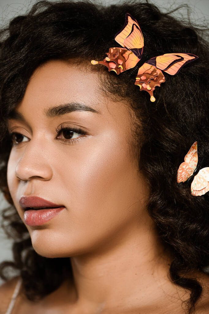 close up de mulher americana africana bonita com borboletas no cabelo posando isolado no cinza - Foto, Imagem