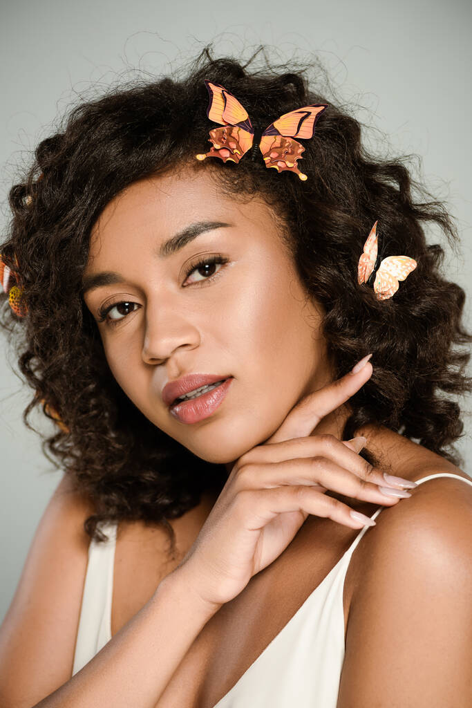 sensuele Afro-Amerikaanse vrouw met vlinders in het haar op zoek naar camera geïsoleerd op grijs - Foto, afbeelding