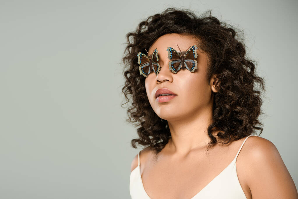 curly african american woman with butterflies on eyes isolated on grey - Photo, Image