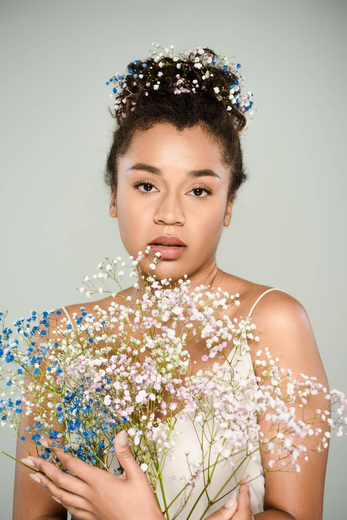 молода афроамериканка з квітучими квітами у волоссі тримає букет з гіпсофіли ізольовані на сірому
 - Фото, зображення