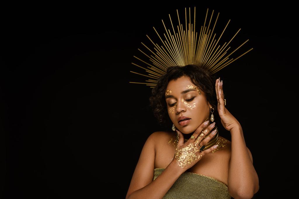 pretty african american woman with golden accessories and paint on face posing isolated on black - Photo, Image