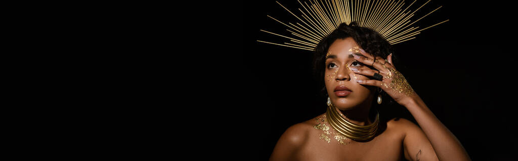 femme afro-américaine tatouée avec couronne dorée et peinture sur le visage regardant isolé sur noir, bannière - Photo, image