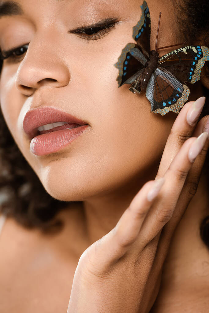 κοντινό πλάνο αισθησιακής και νεαρής αφροαμερικάνας γυναίκας με πεταλούδα στο μάγουλο  - Φωτογραφία, εικόνα