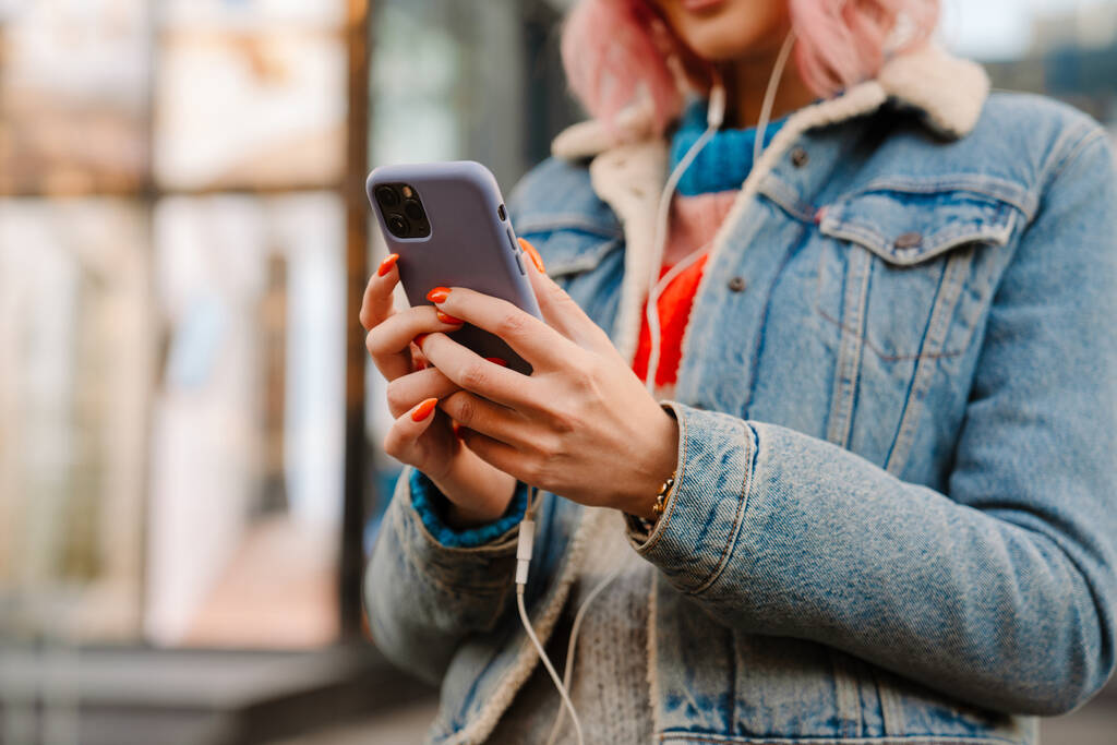 Молодая белая женщина в наушниках с помощью мобильного телефона на городской улице - Фото, изображение