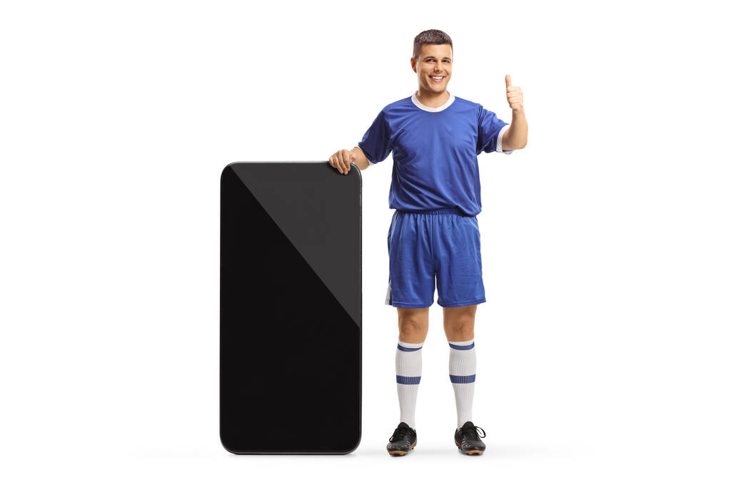 Чоловік у футбольній майці стоїть поруч з великим смартфоном і показує великі пальці вгору ізольовано на білому тлі
 - Фото, зображення