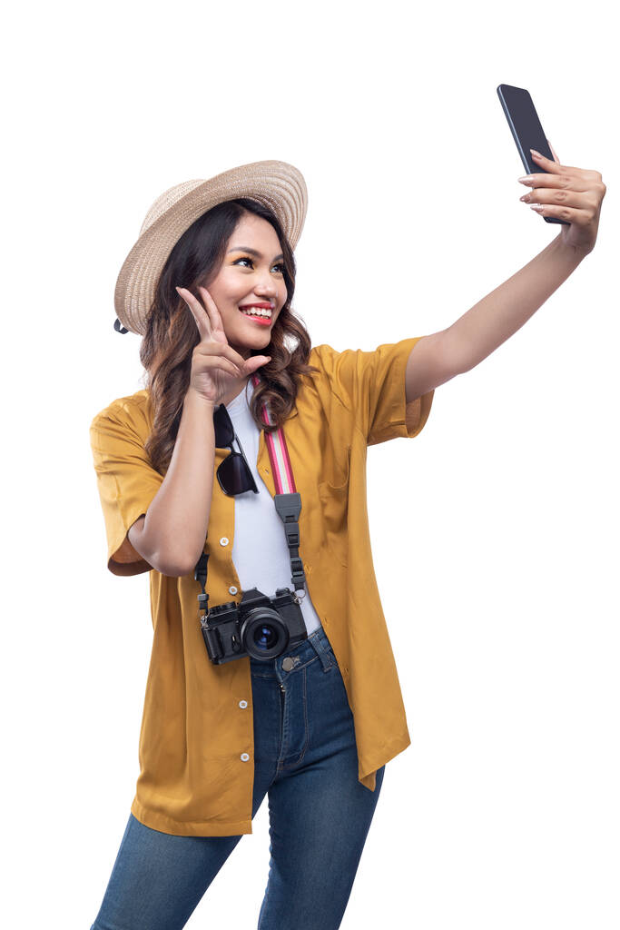 Mujer asiática con sombrero y cámara tomando una selfie con un teléfono móvil aislado sobre fondo blanco - Foto, Imagen