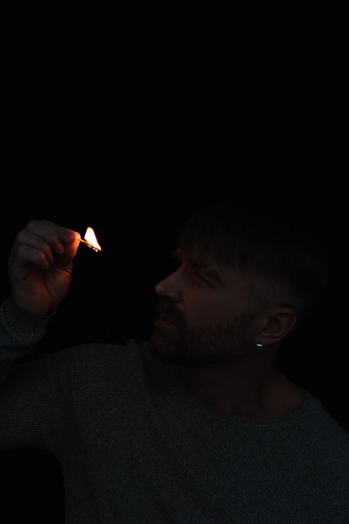 man kijkt naar vlam van brandende lucifer tijdens stroomuitval geïsoleerd op zwart - Foto, afbeelding