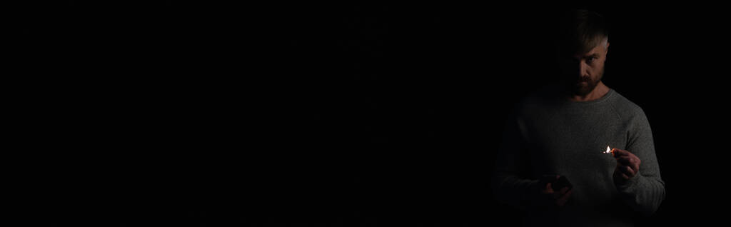 elégedetlen férfi gyufásdobozzal és égő gyufával nézi a kamerát a fekete zászlón elszigetelt áramszünet alatt. - Fotó, kép