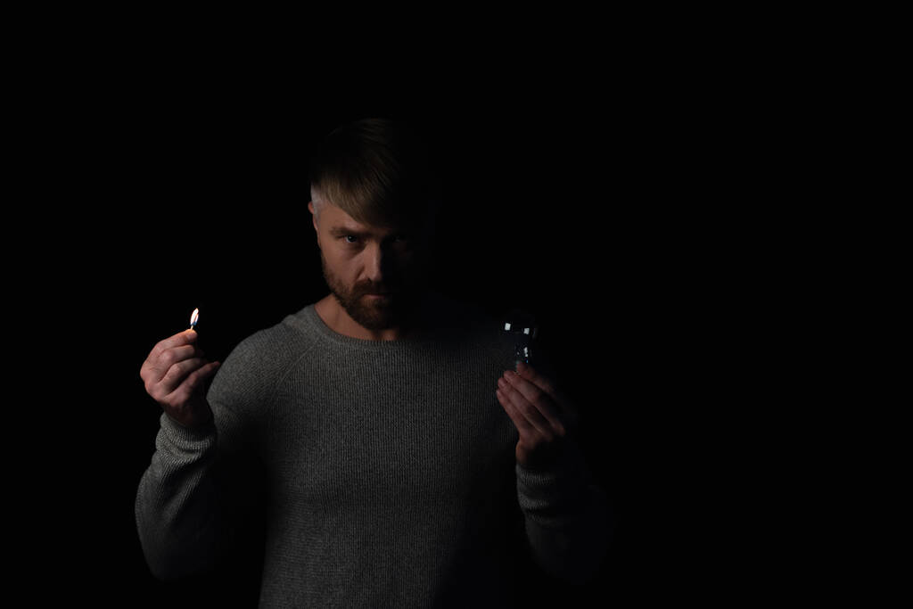 irritált férfi villanykörte és égő gyufa néz kamera elszigetelt fekete - Fotó, kép