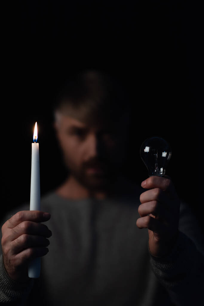 電球と燃えるろうそくの選択的焦点黒で隔離されたぼやけた男の手に - 写真・画像