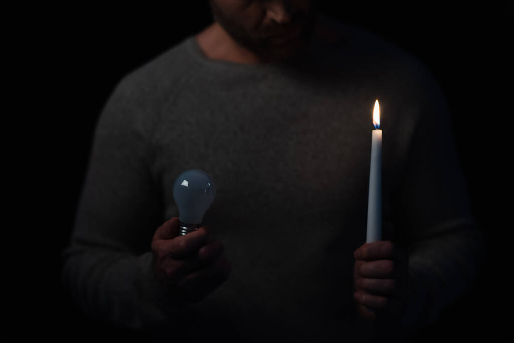 partial view of man with burning candle and light bulb isolated on black - Photo, Image