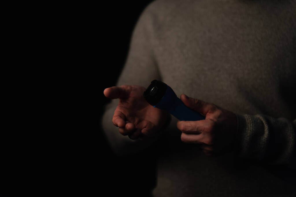 cropped view of man in darkness holding electric flashlight isolated on black - Photo, Image